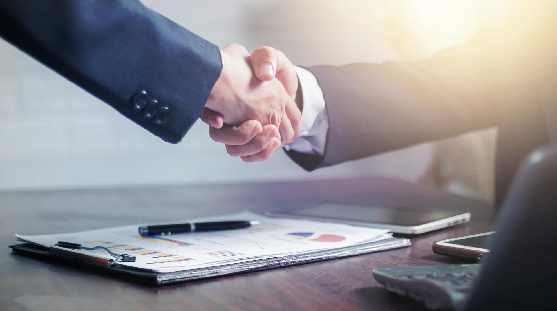 Professional handshake agreement over business charts in an office setting.