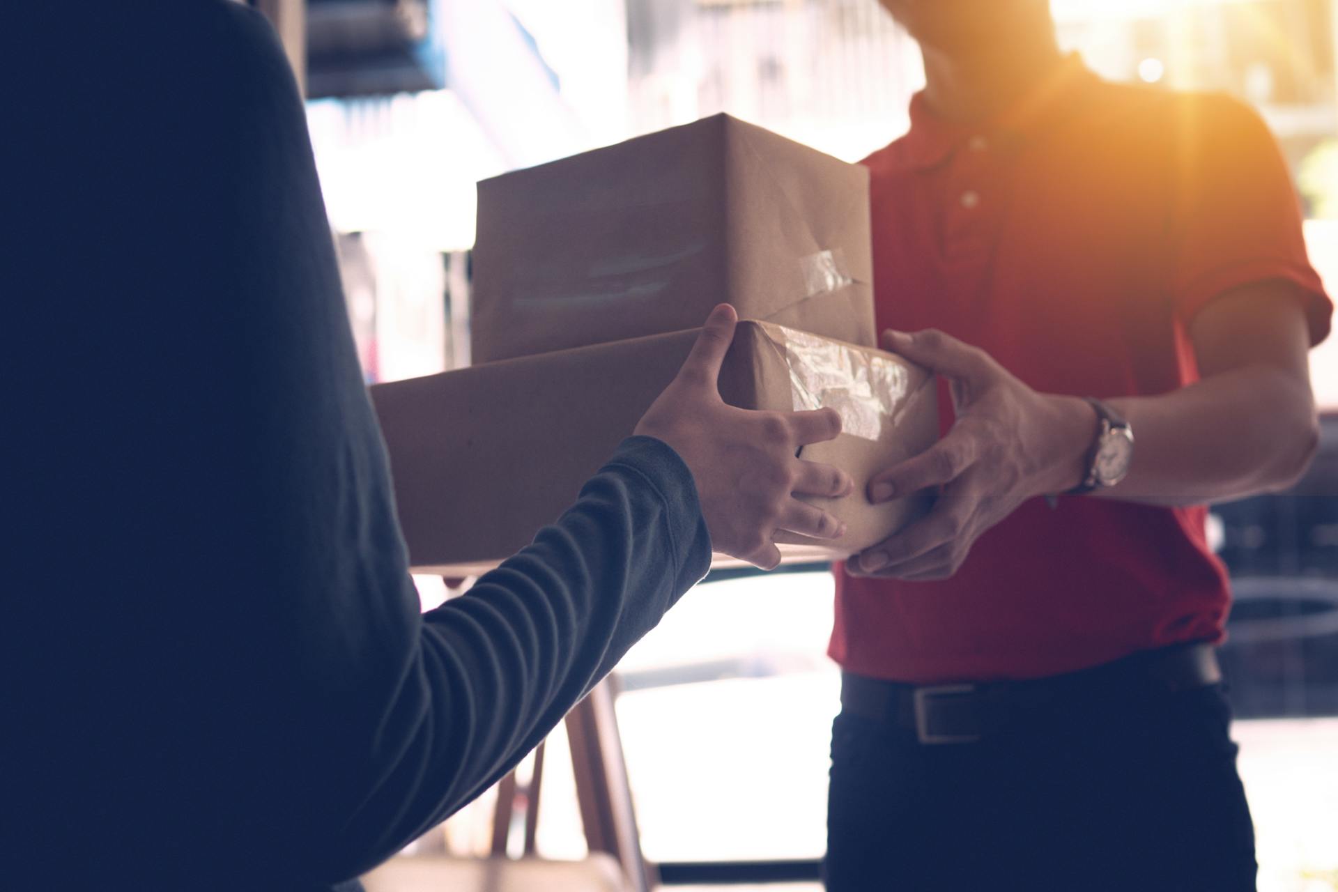 Close-up of a delivery service worker handing over packages to a customer indoors.