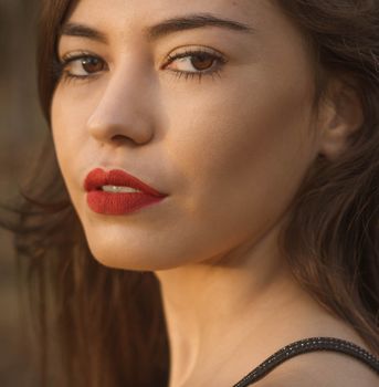 Closeup of gentle crop young female with red lipstick and brown eyes looking at camera
