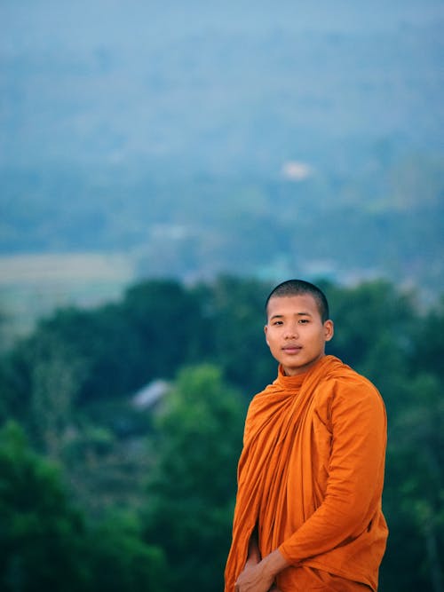 Young Man in Orange Robe Standing With View Of Nature Behind