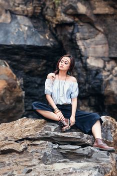 Stylish Asian woman in a trendy outfit posing on rocks in Bandung, showcasing fashion outdoors.