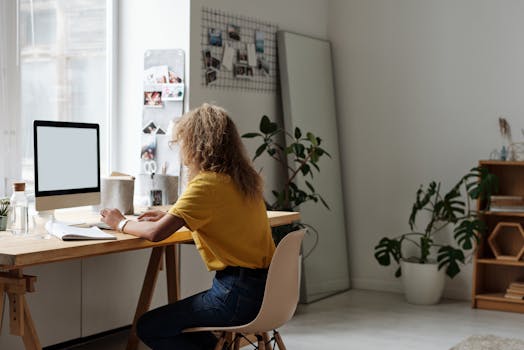 Woman working on a computer in a stylish home office, surrounded by plants and decor.