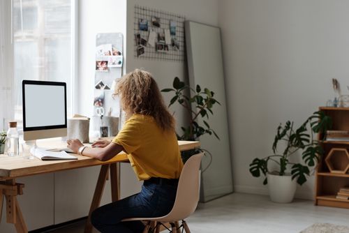 Free Woman working on a computer in a stylish home office, surrounded by plants and decor. Stock Photo
