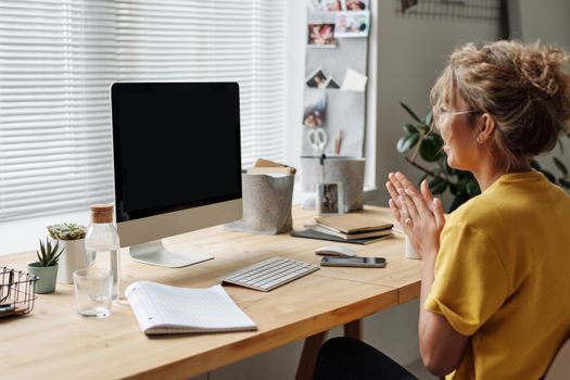 A woman in a yellow shirt video chatting from her cozy home office.