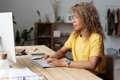 Free A woman working remotely from home, typing on a keyboard at her work desk. Stock Photo