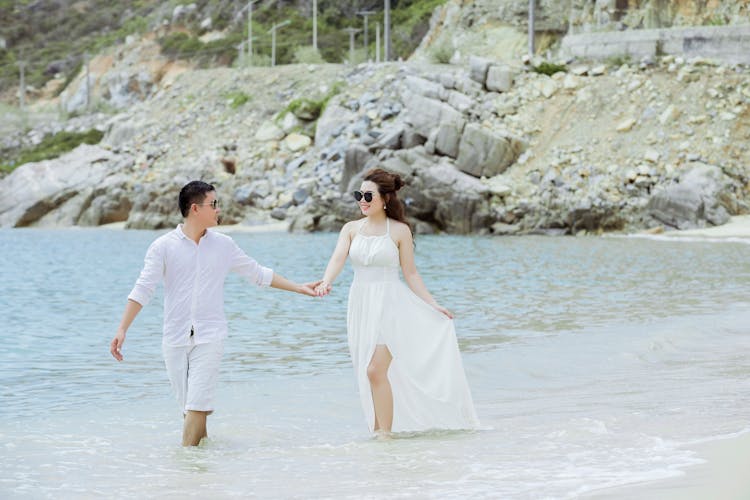 Smiling Ethnic Couple Walking On Ocean Beach During Summer Vacation