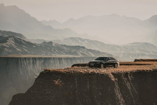 Scenery view of high rough ridge in mist and contemporary style black automobile on dry uneven surface in daytime