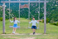 Happy Asian friends swinging above grass near ridge with trees