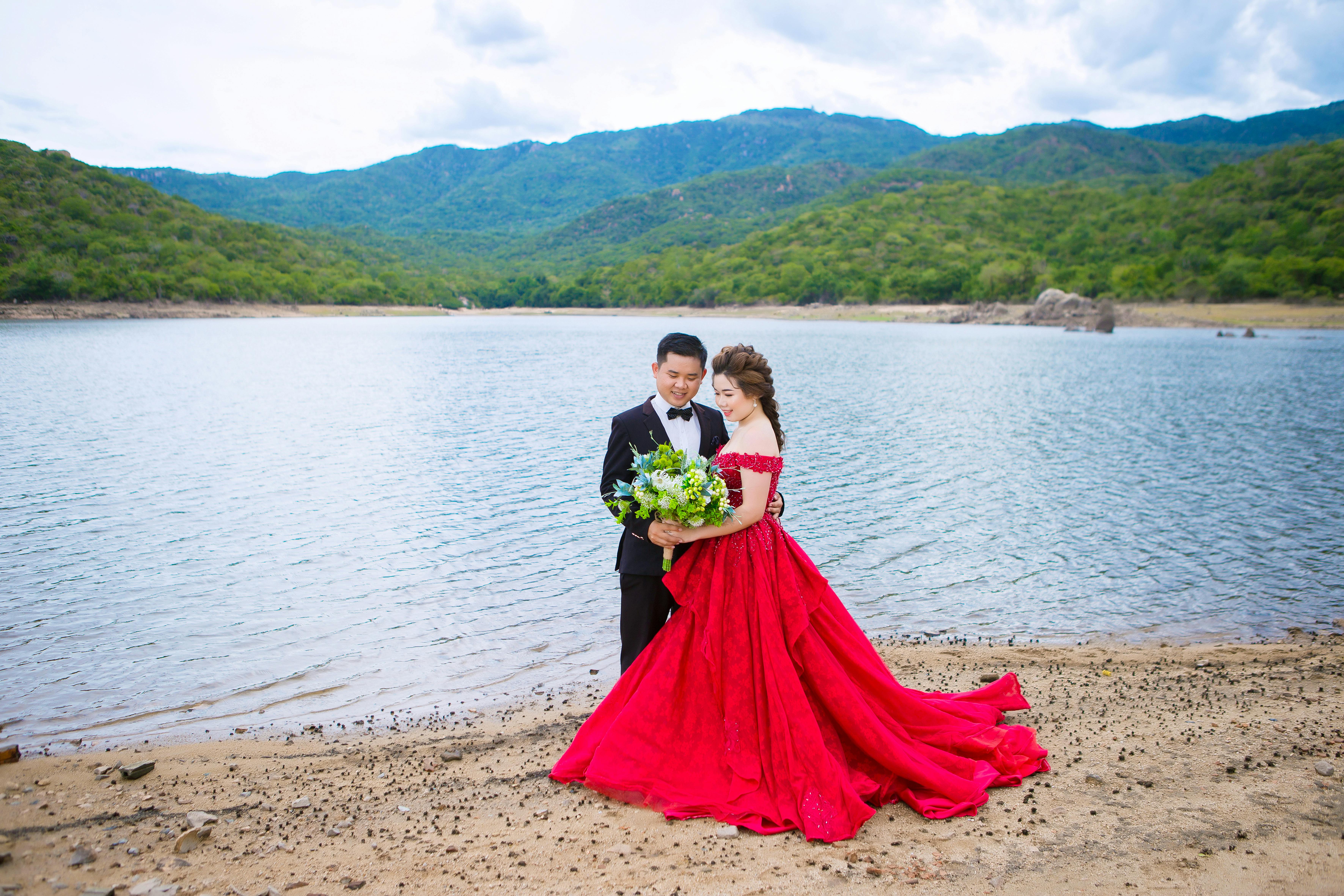 elegant newlywed couple with bridal bouquet near pond and mountains