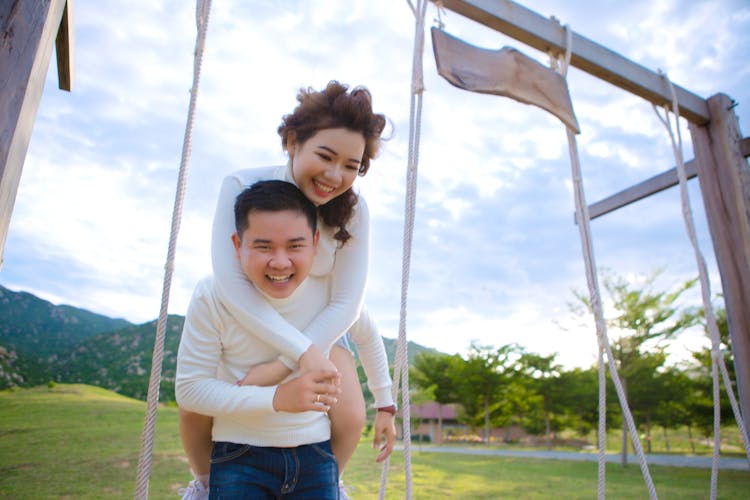 Happy Man Carrying Positive Ethnic Wife On Back Near Swing