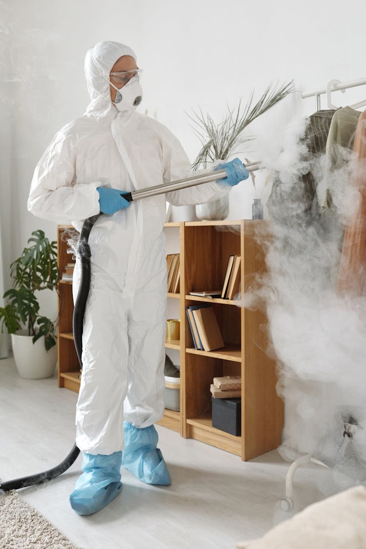 A Woman In A Protective Suit Disinfecting Clothes 