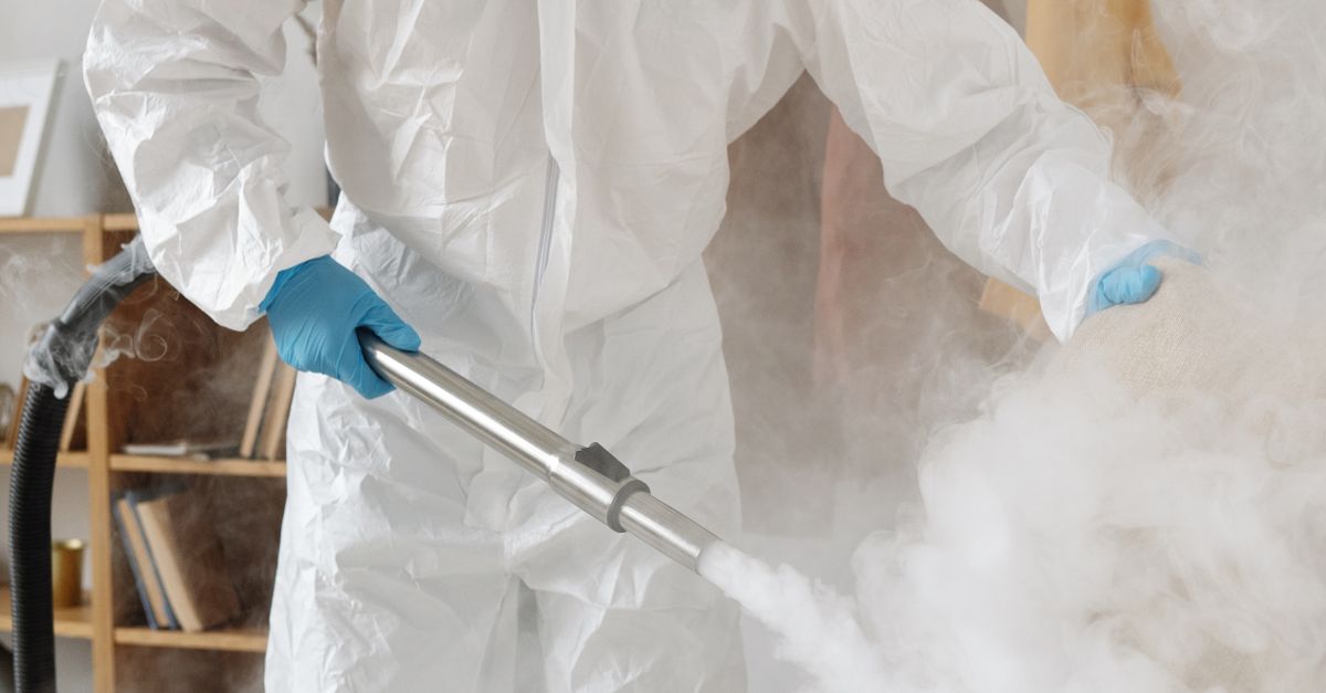 Photo by Michelangelo Buonarroti Person in PPE fumigates indoors with protective suit, gloves, and mask.