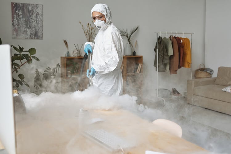 A Woman In Protective Suit Disinfecting A Table 