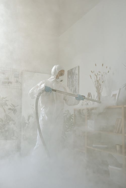 person in white coveralls and mask fumigating a room