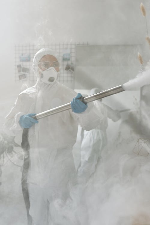 A Woman in Disinfecting While in a Protective Suit 