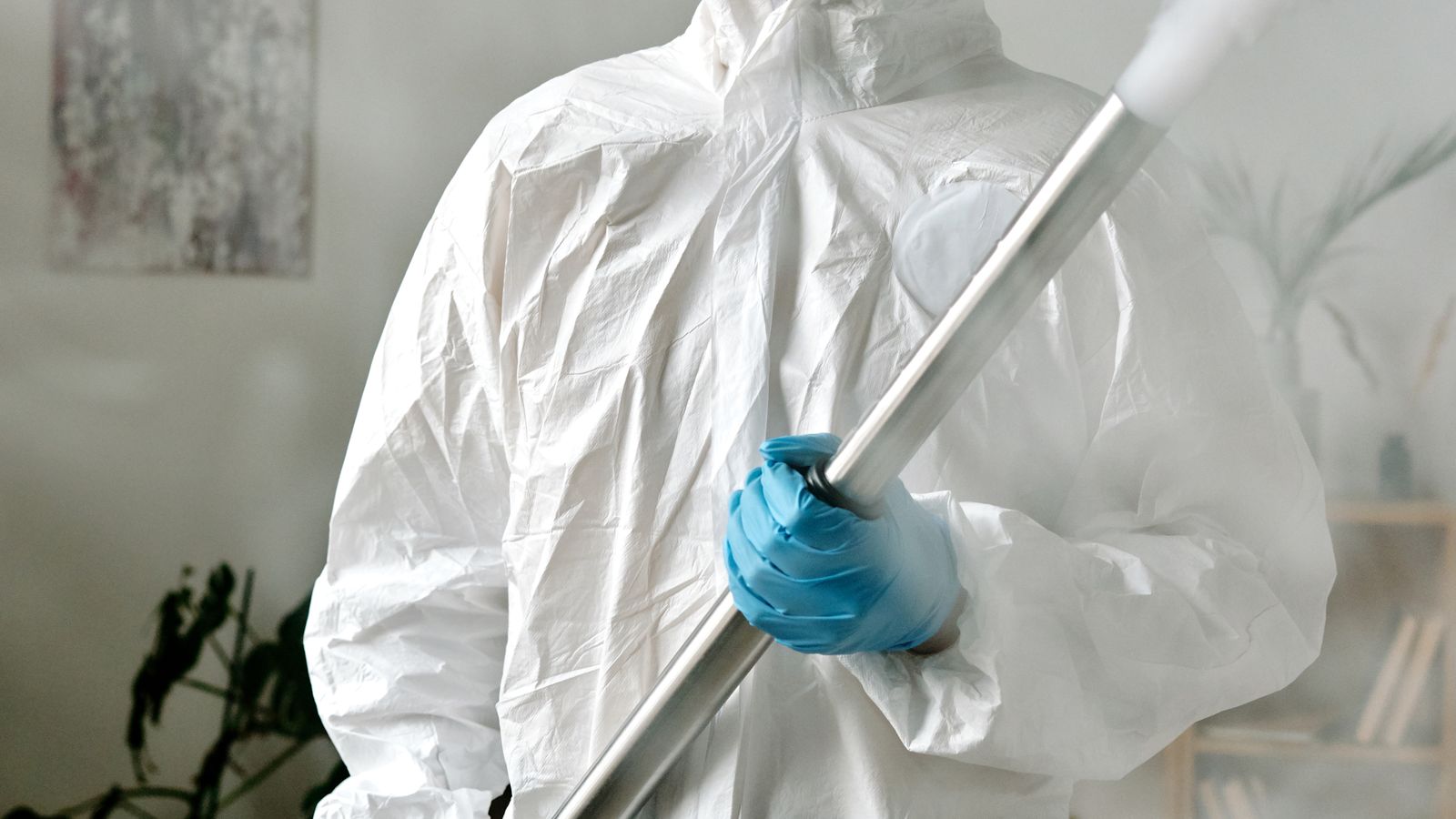 Intervenant en combinaison de protection intégrale manipulant un appareil de nébulisation dans une pièce vide.