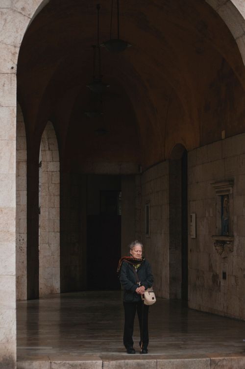 Free Elderly woman stands under archway in Pisa, exhibiting a classic architectural charm. Stock Photo