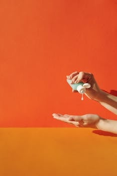 Hands applying sanitizer against vibrant orange backdrop, emphasizing hygiene.