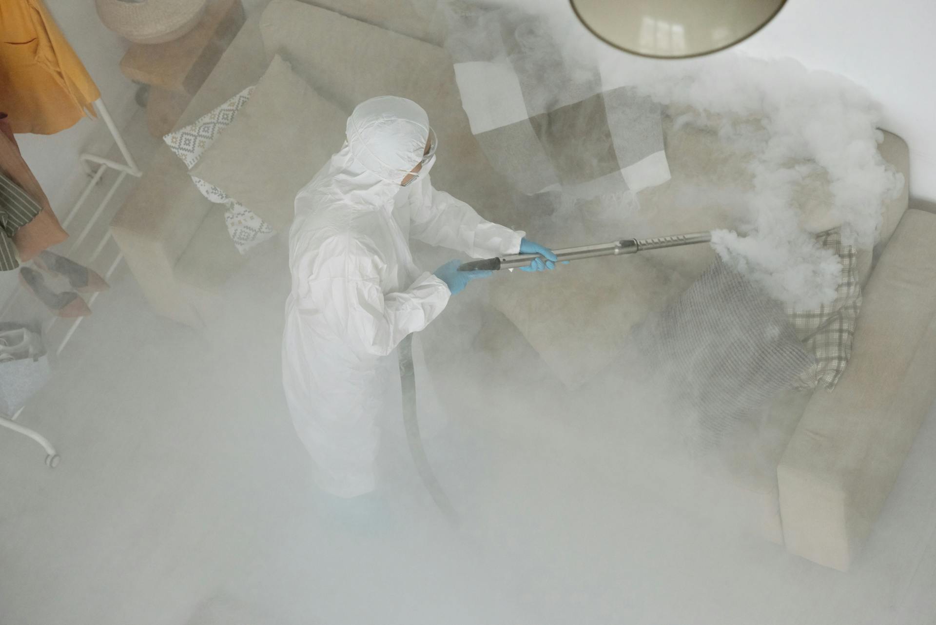 Person in White Protective Clothing Fumigating a Couch