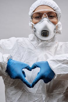 Healthcare worker in full protective gear making a heart symbol with gloved hands.