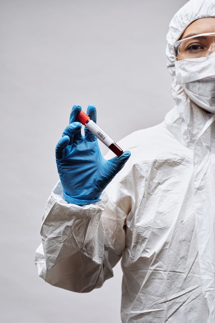 Person Wearing Protective Clothing And Blue Gloves Holding A Test Tube