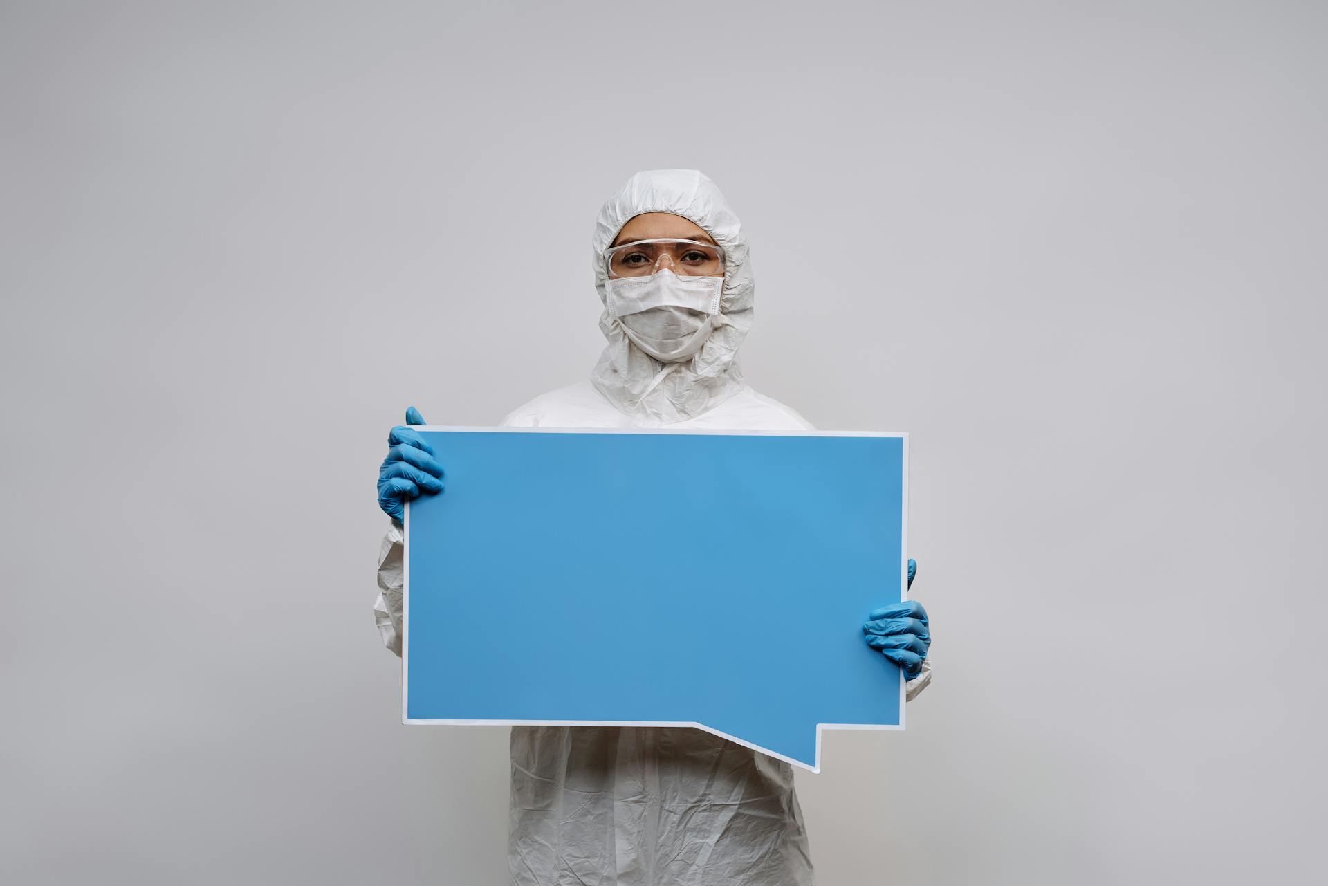 Person in White Personal Protective Equipment Holding a Blank Signage