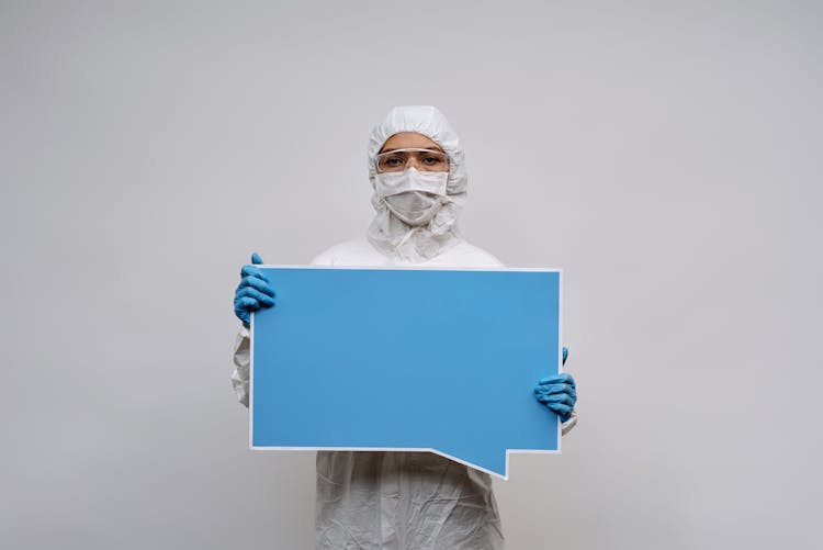 Person In White Personal Protective Equipment Holding A Blank Signage