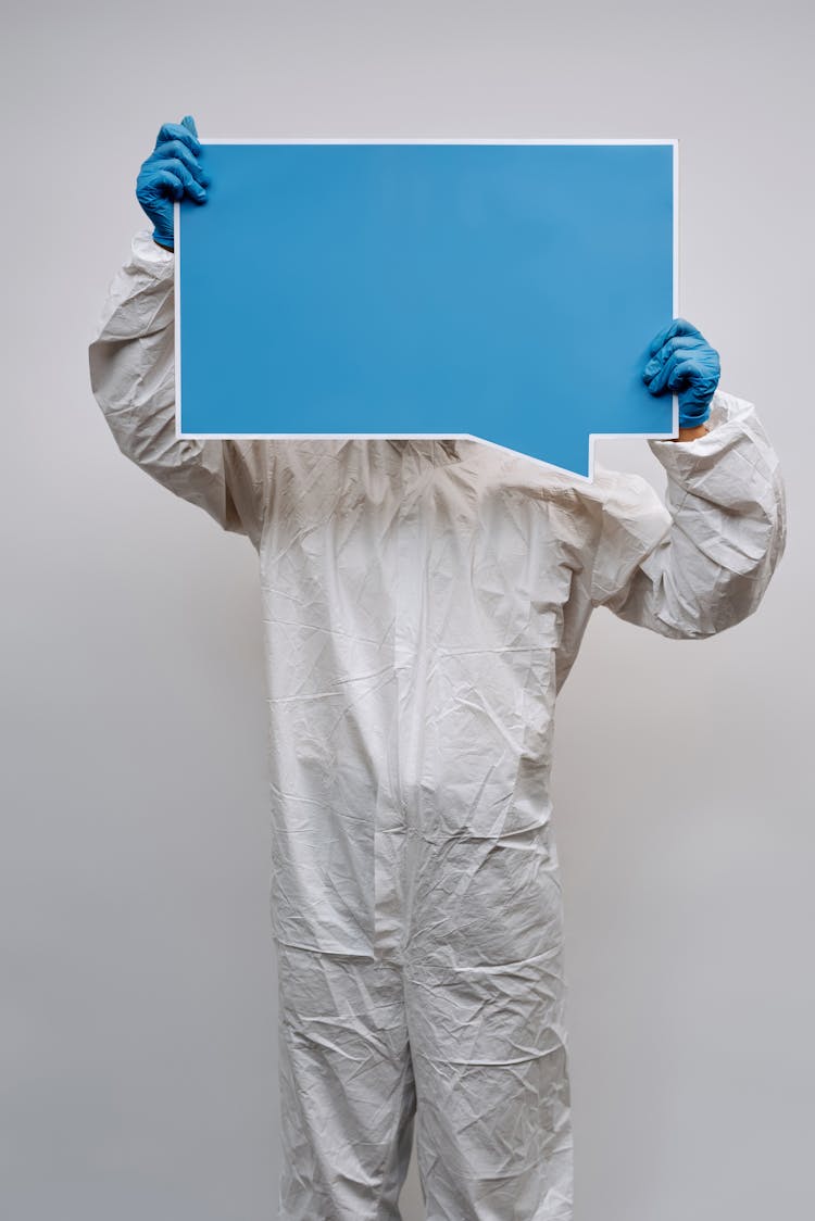 Person In White Protective Clothing And Gloves Holding A Signage Covering Face