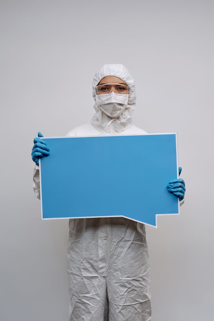 Person In White Personal Protective Equipment Holding Blue And White Blank Signage