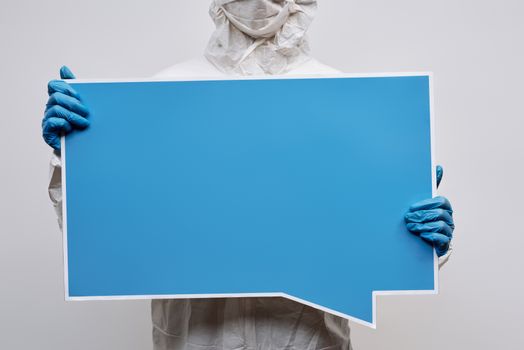 A person wearing protective gear holding a large blue speech bubble placard with copy space.