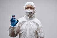 科学家将血液样本放入灰色背景下的试管中，身着防护装备