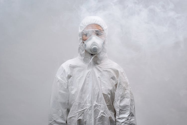 Person In White Coveralls And Mask Standing In A Smoky Room