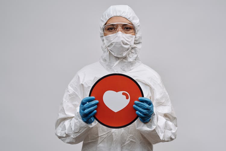 Person In White Coveralls And Mask Holding A Red Signage