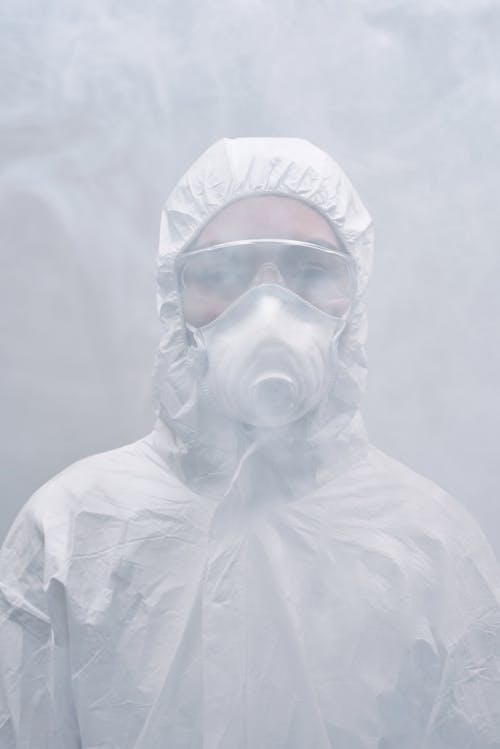 Person in White Protective Clothing and Mask Standing in Smoke