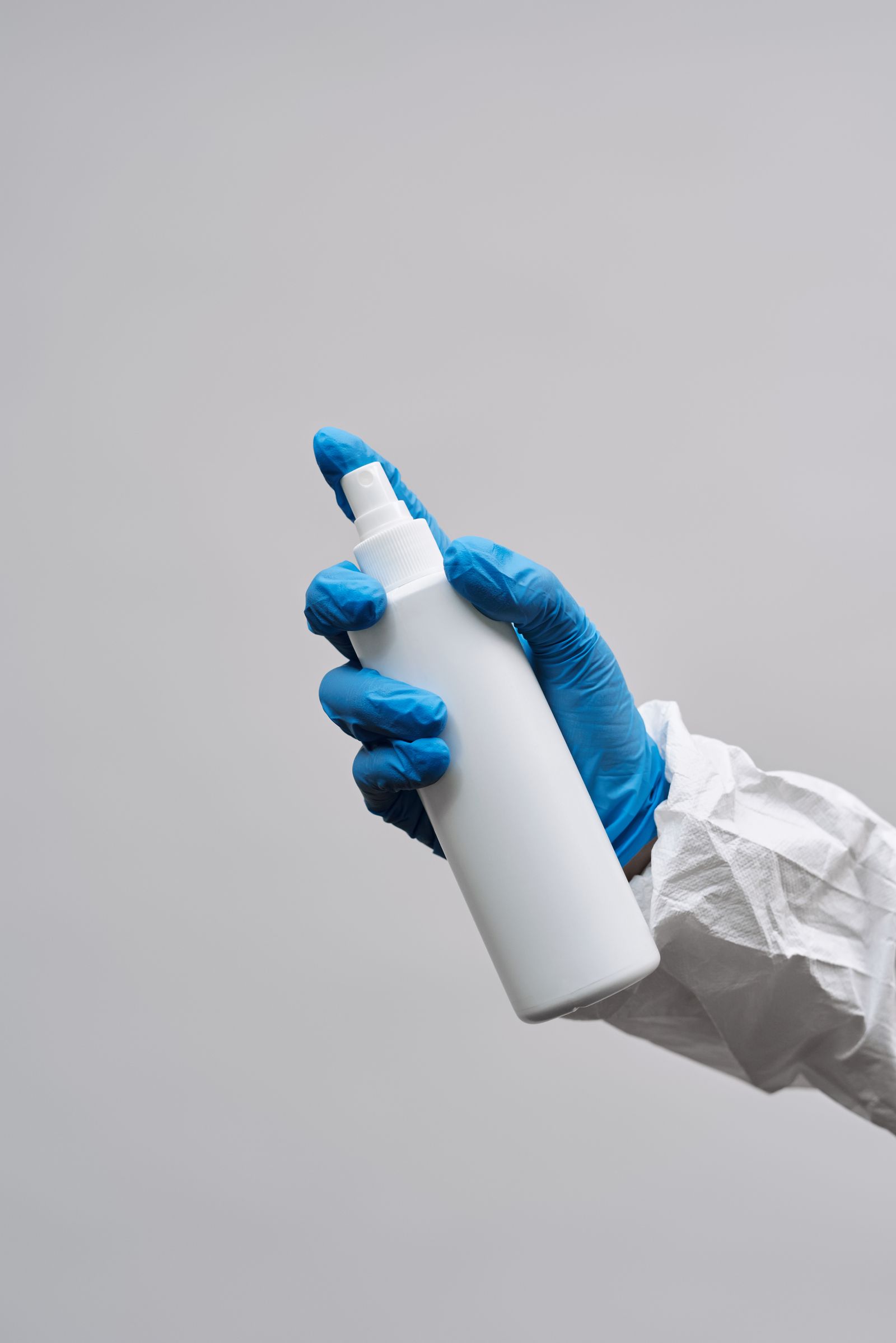 Mains gantées avec un flacon de produit pour la désinfection des surfaces