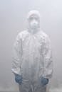 大雾中，一个穿着全套防护装备、戴着口罩的人站在那里