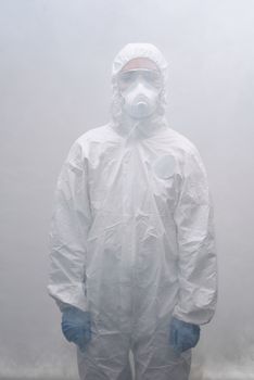 大雾中，一个穿着全套防护装备、戴着口罩的人站在那里