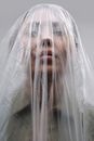 Serious unrecognizable adult female in khaki color clothes covered with plastic bag standing on grey background