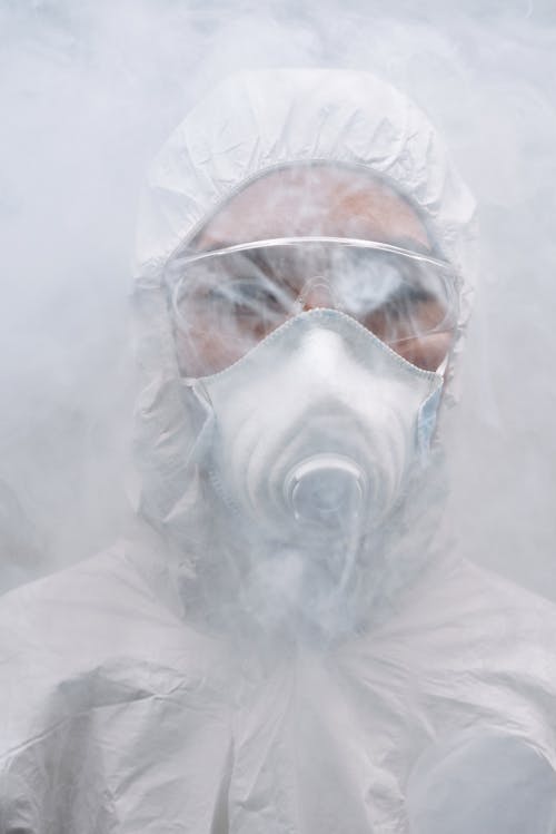 Person Wearing White coveralls and Mask Standing in Fog