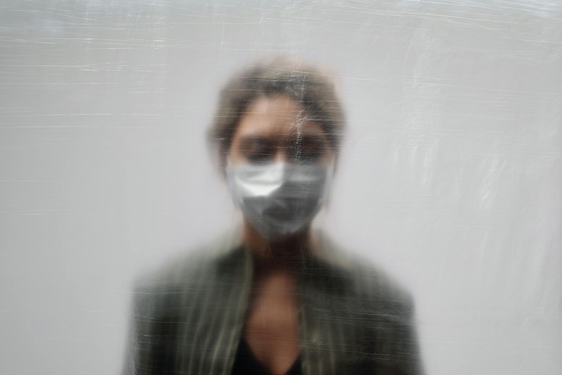 Woman Wearing a Face Mask and Green Top Behind a Clear Plastic Sheet