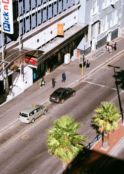 阳光明媚，城市街景充满活力，汽车、棕榈树和行人随处可见