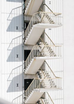 现代楼梯的高台阶上，阳光照耀着建筑白色墙壁旁的金属栏杆