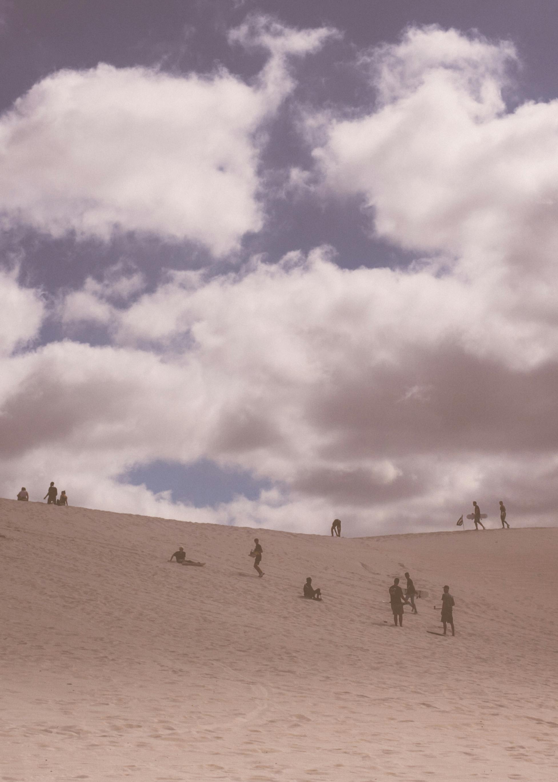 People exploring sand dunes under a cloudy sky, depicting leisure and adventure outdoors.