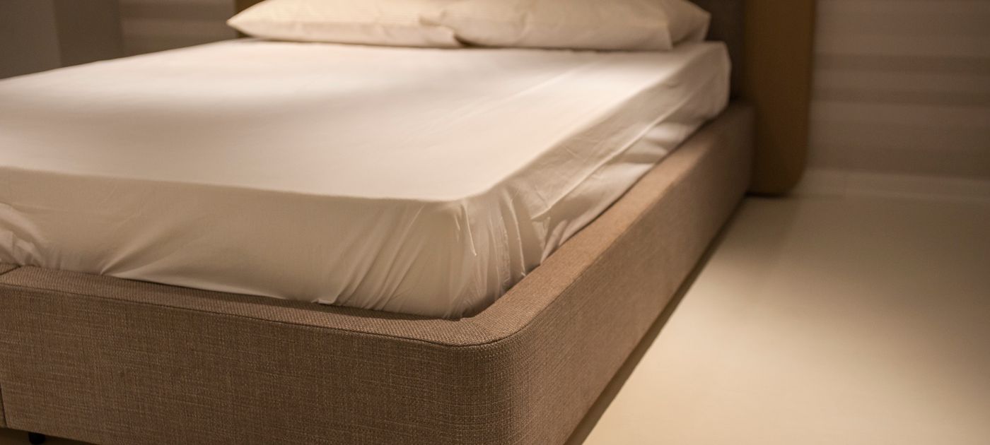 A bed with white linen sheets — the mattress seams are where bed bugs hide and leave their signs