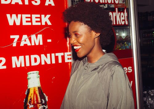 Side view of laughing African American female in outerwear standing near advertising space in supermarket looking away