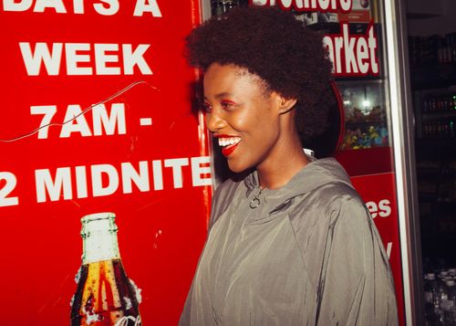 Free Side view of laughing African American female in outerwear standing near advertising space in supermarket looking away Stock Photo
