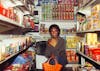Free Happy black female in casual clothes with shopping bag demonstrating product squatting among grocery shelves while choosing goods in supermarket Stock Photo