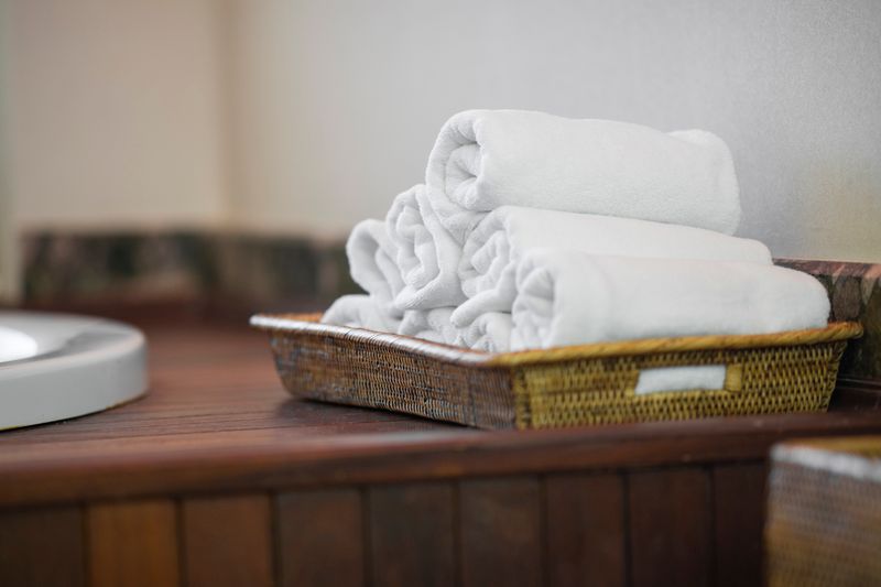 Rolled white towels neatly placed in a woven basket, perfect for spa or bathroom decor.