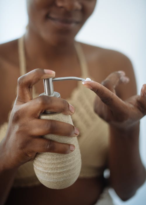 Crop woman with pump bottle of cream in bathroom