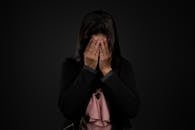 一位深色头发、穿着休闲服的悲伤女性，在黑色背景前用手遮住了脸